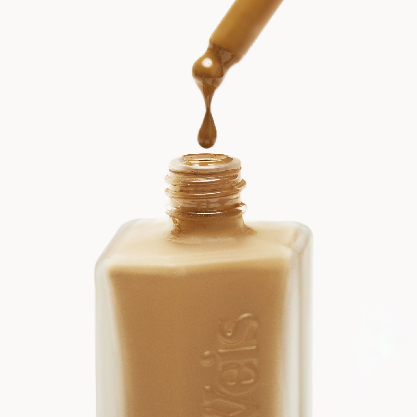 Close up of the top of a frosted glass liquid foundation bottle with liquid foundation being dropped back in from the pipette