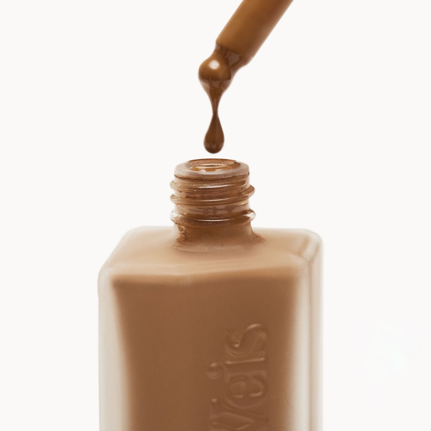 Close up of the top of a frosted glass liquid foundation bottle with liquid foundation being dropped back in from the pipette