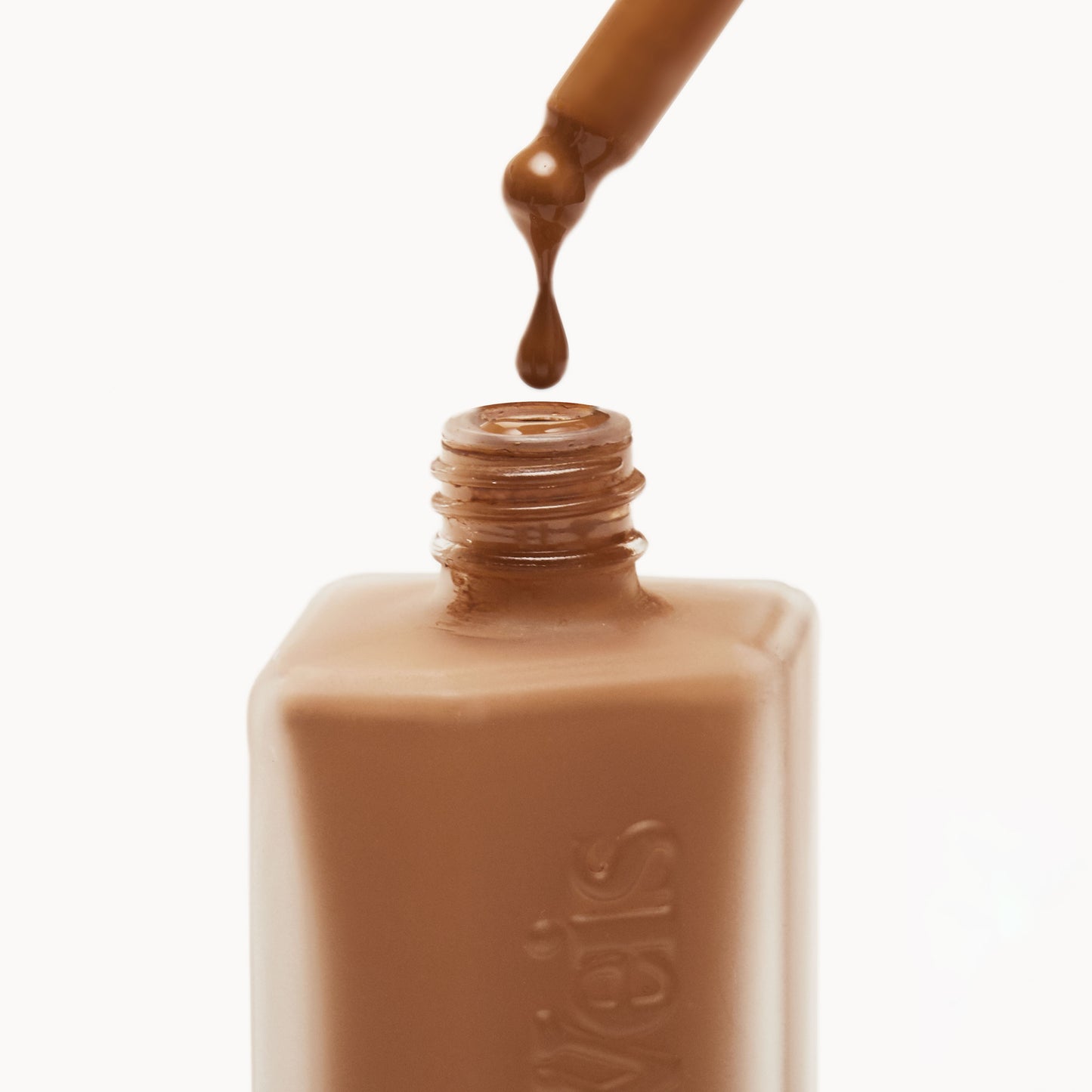 Close up of the top of a frosted glass liquid foundation bottle with liquid foundation being dropped back in from the pipette