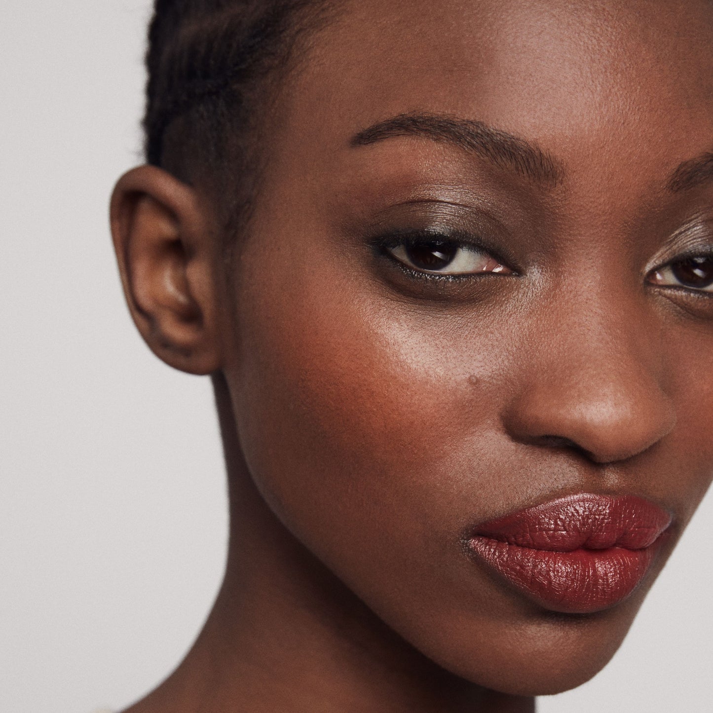 Close up of a person’s face with a deep skin tone wearing cream blush