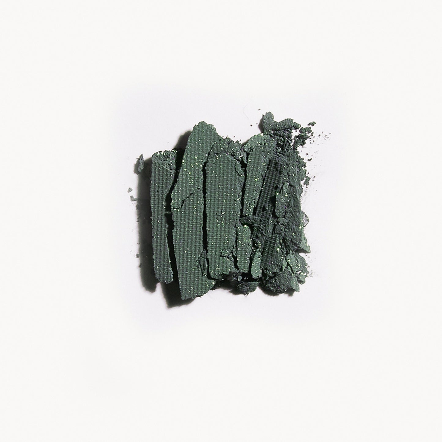 Crumbled up green eye shadow with gold flecks on a white background