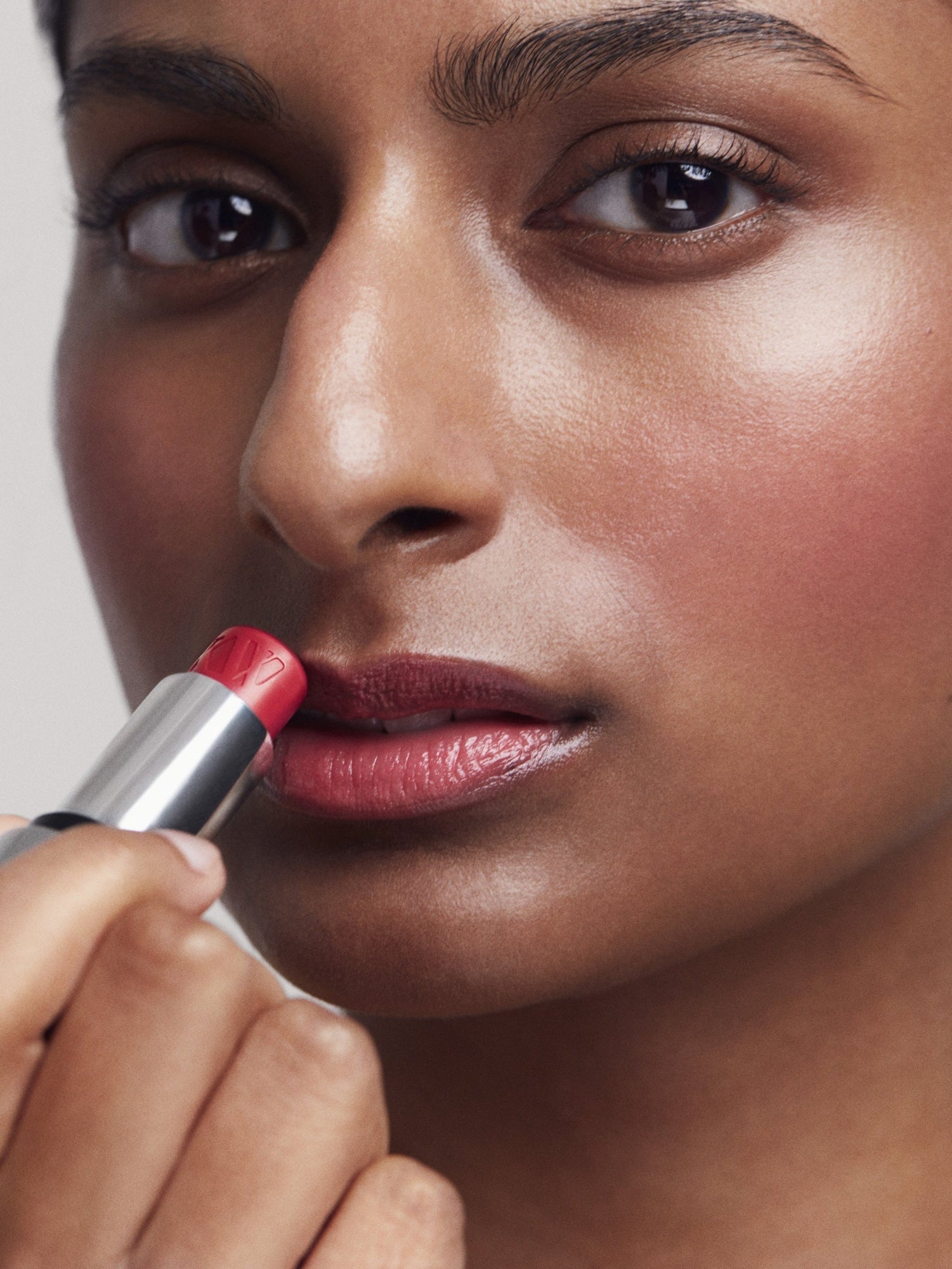 Close-up of a person applying red Tinted Lip Balm with a neutral background
