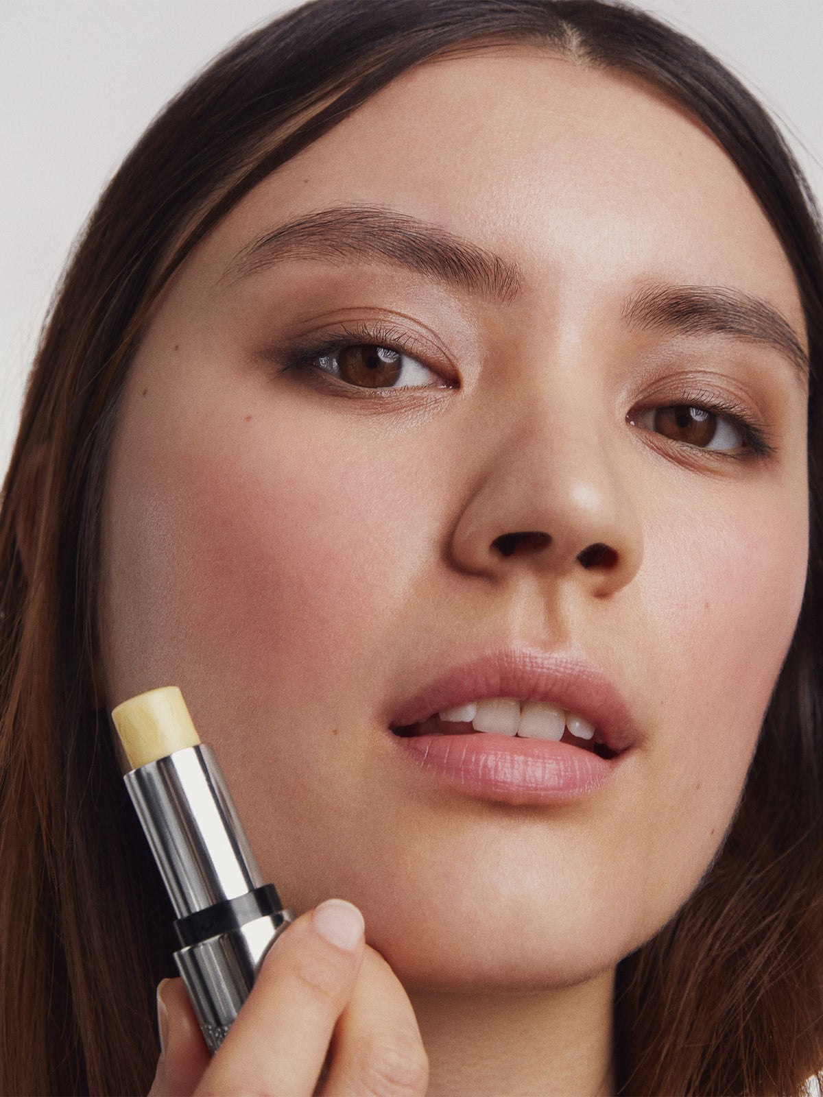 Close-up of a person holding clear Tinted Lip Balm with a neutral background