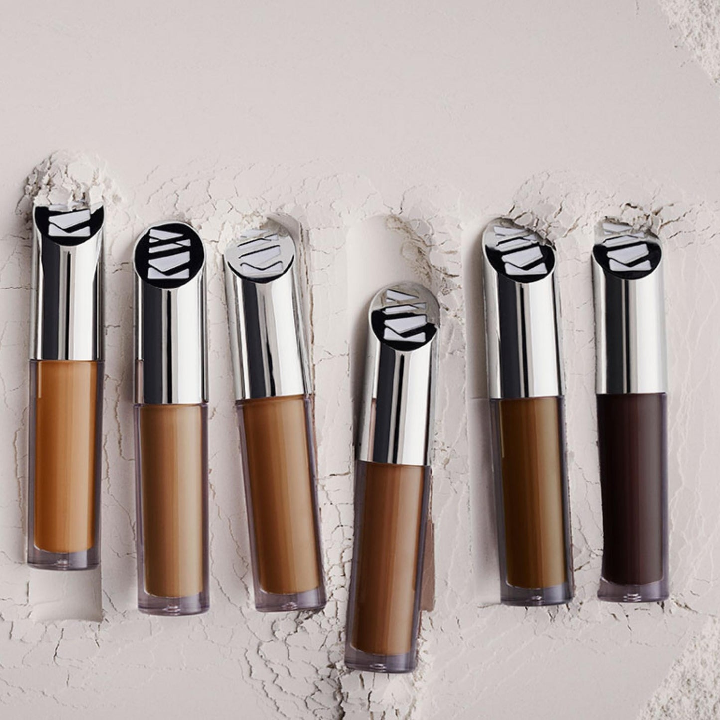 Six bottles of concealer in different shades, embedded in a white powder