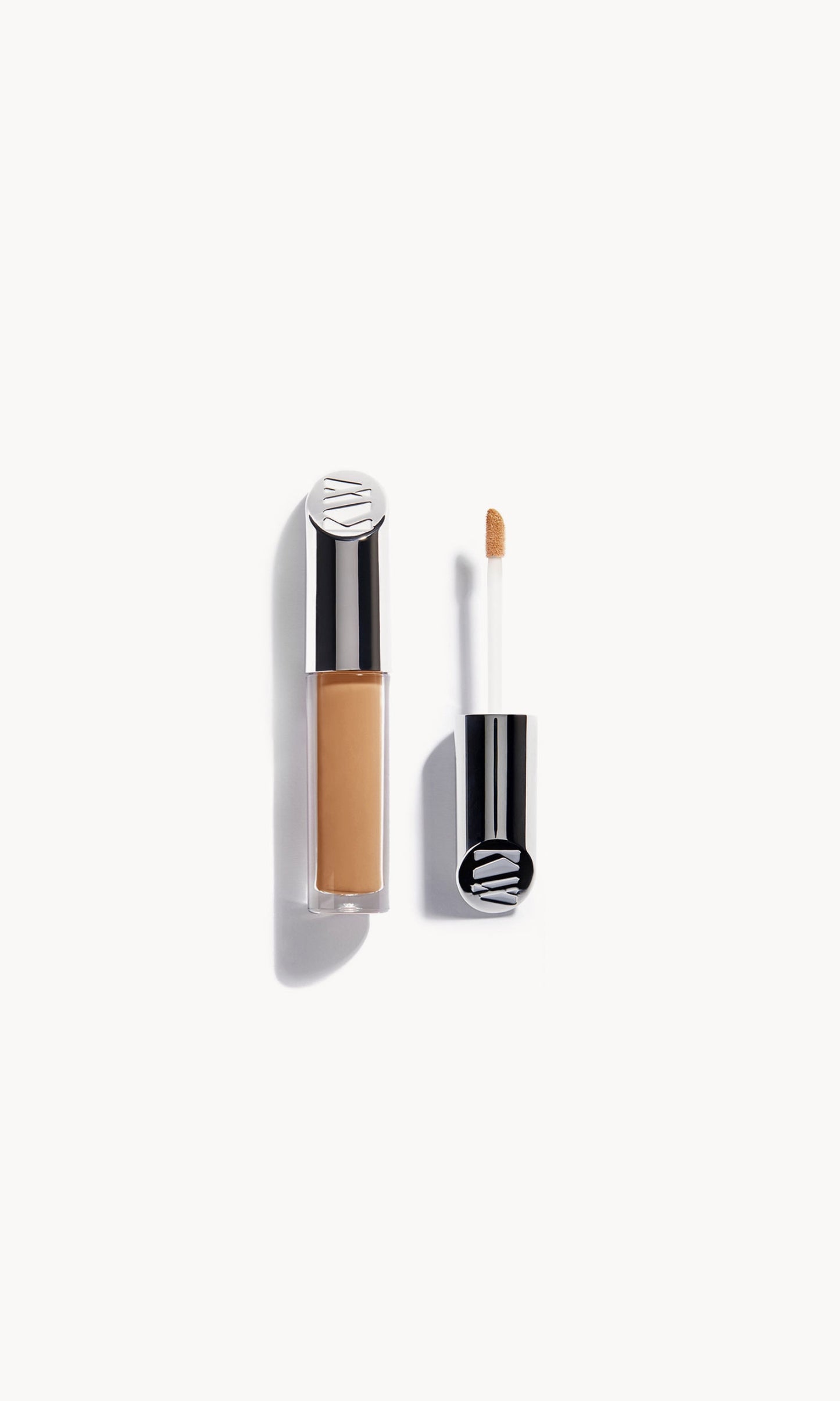 Kjaer Weis concealer in a clear bottle with silver metal top next to the concealer wand