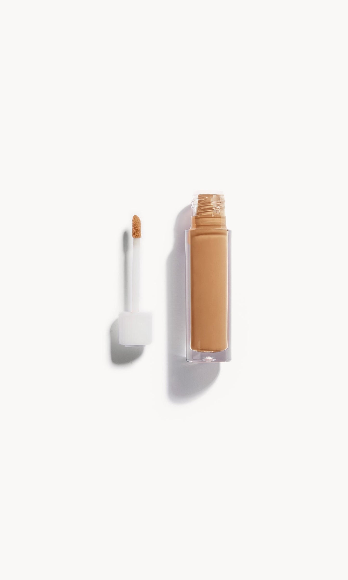 An open bottle of concealer on its side next to a white refill wand