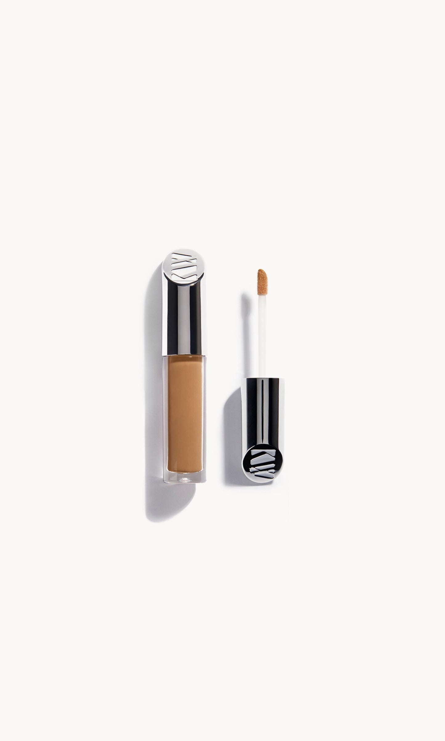Kjaer Weis concealer in a clear bottle with silver metal top next to the concealer wand
