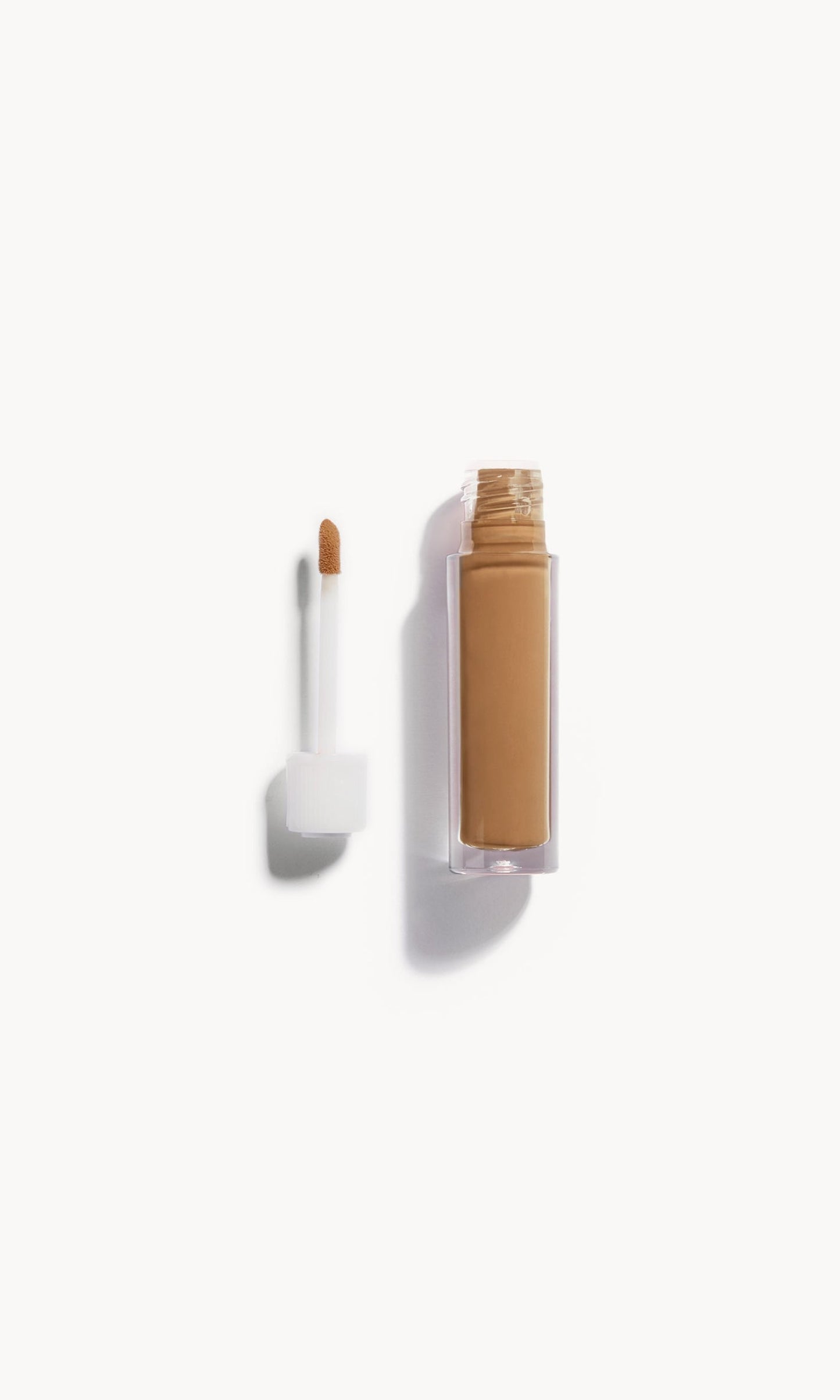 Alt text: An open bottle of concealer on its side next to a white refill wand