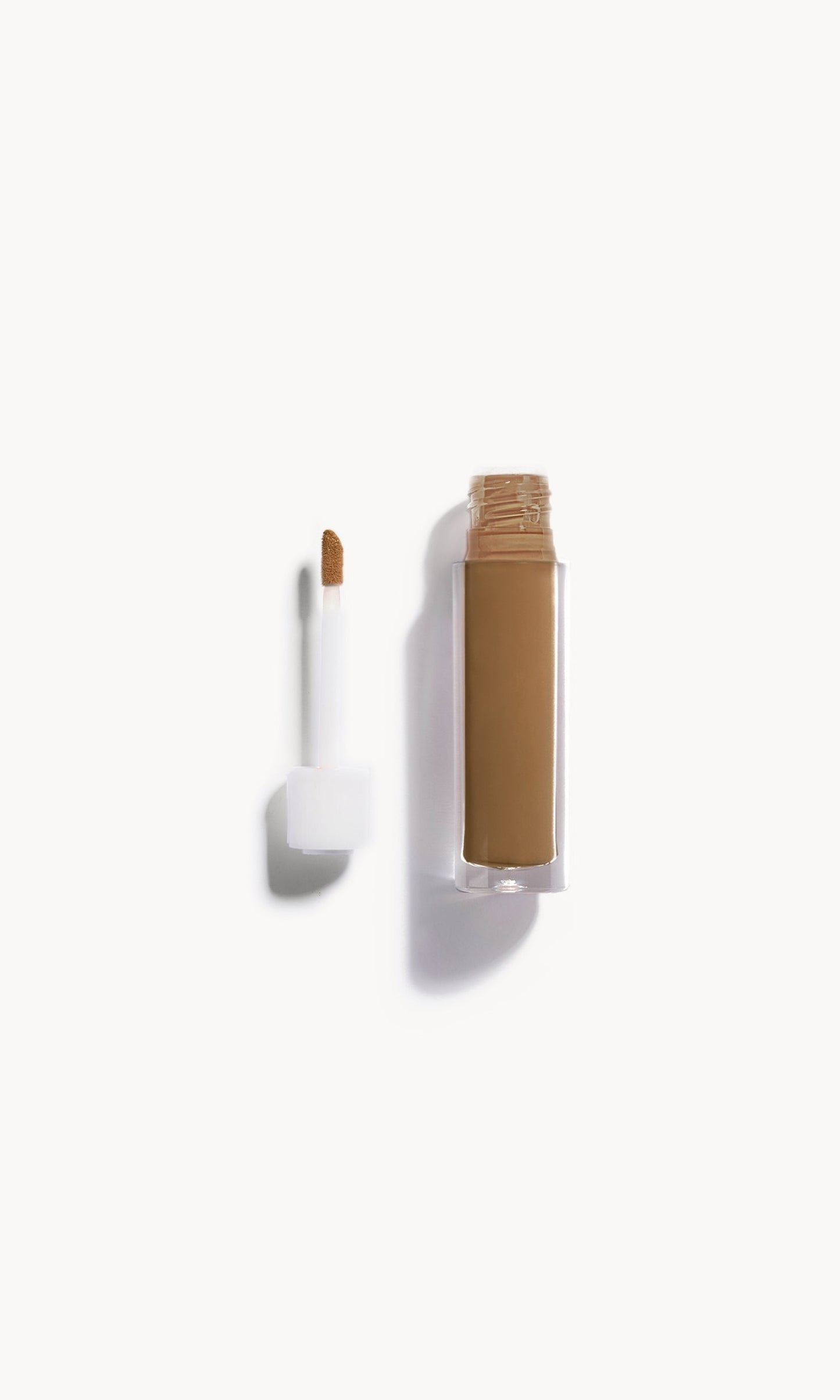 An open bottle of concealer on its side next to a white refill wand