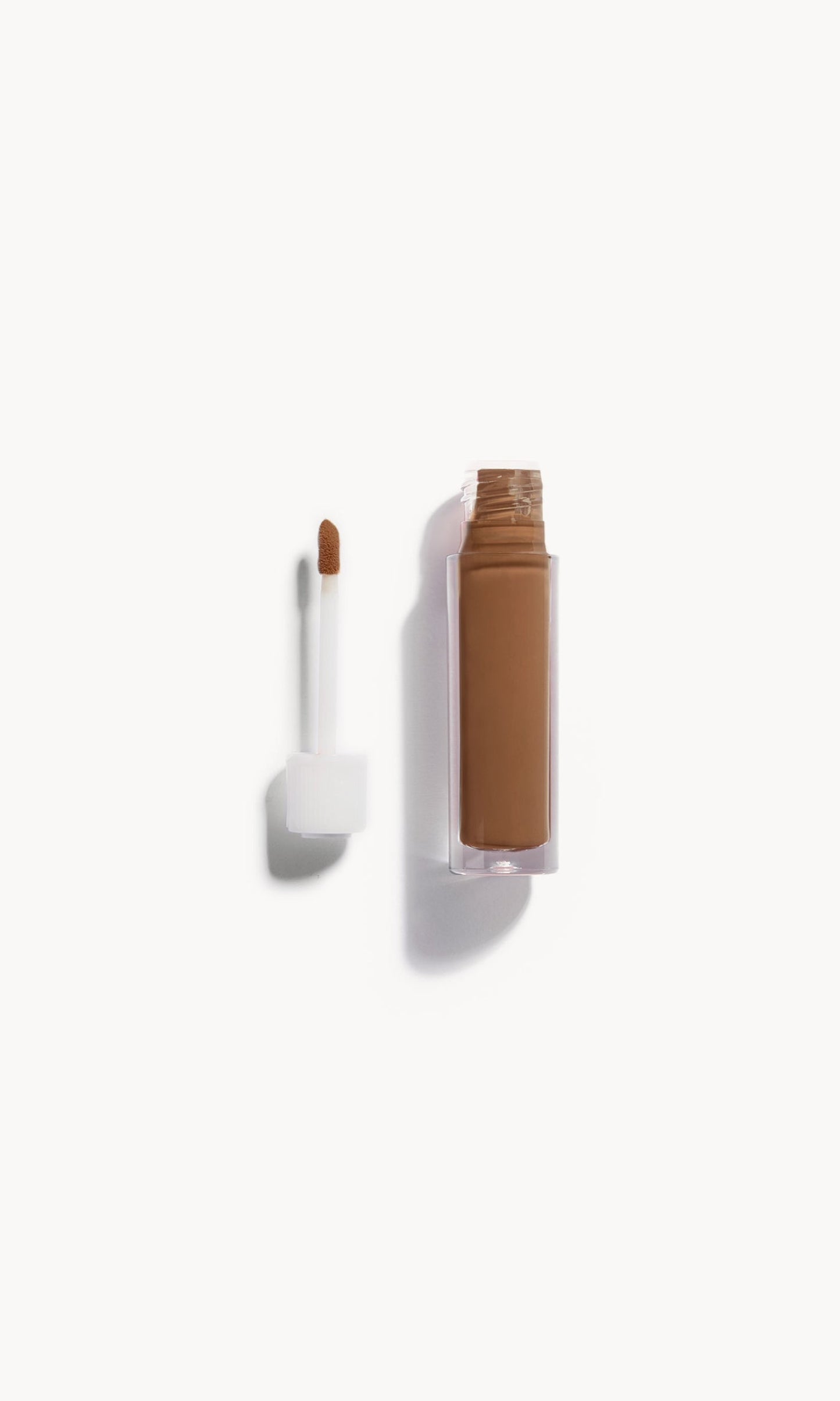 An open bottle of concealer on its side next to a white refill wand