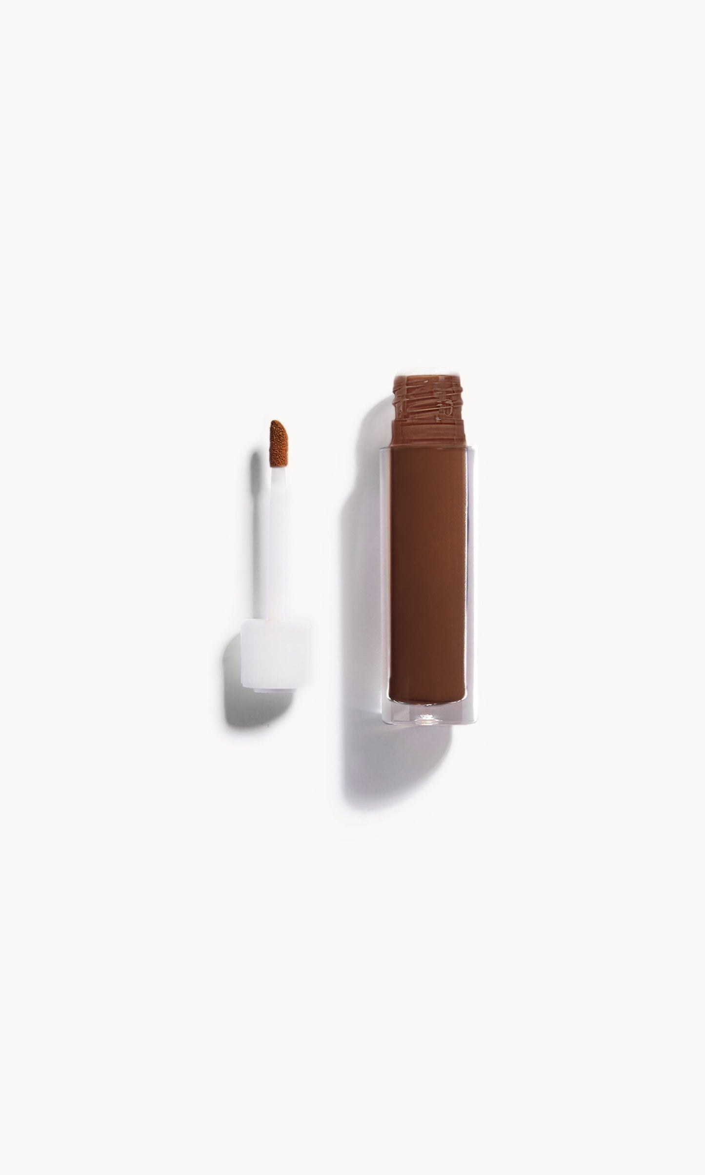An open bottle of concealer on its side next to a white refill wand