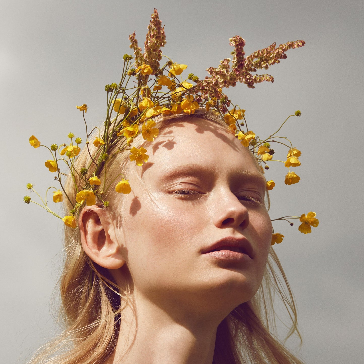 Close up of a person’s face with a fair skin tone wearing cream blush and a yellow flower crown