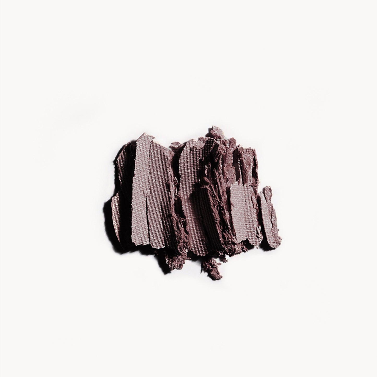 Crumbled up greyish purple eye shadow on a white background