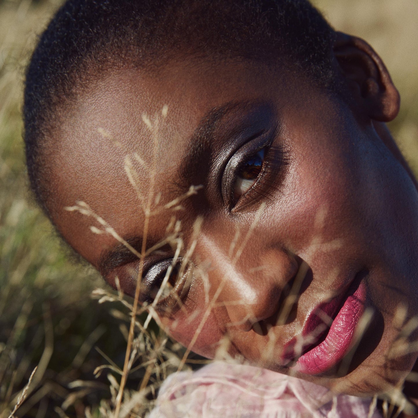 Close up of a person’s face lying in grass wearing black eyeshadow with a silver shimmer