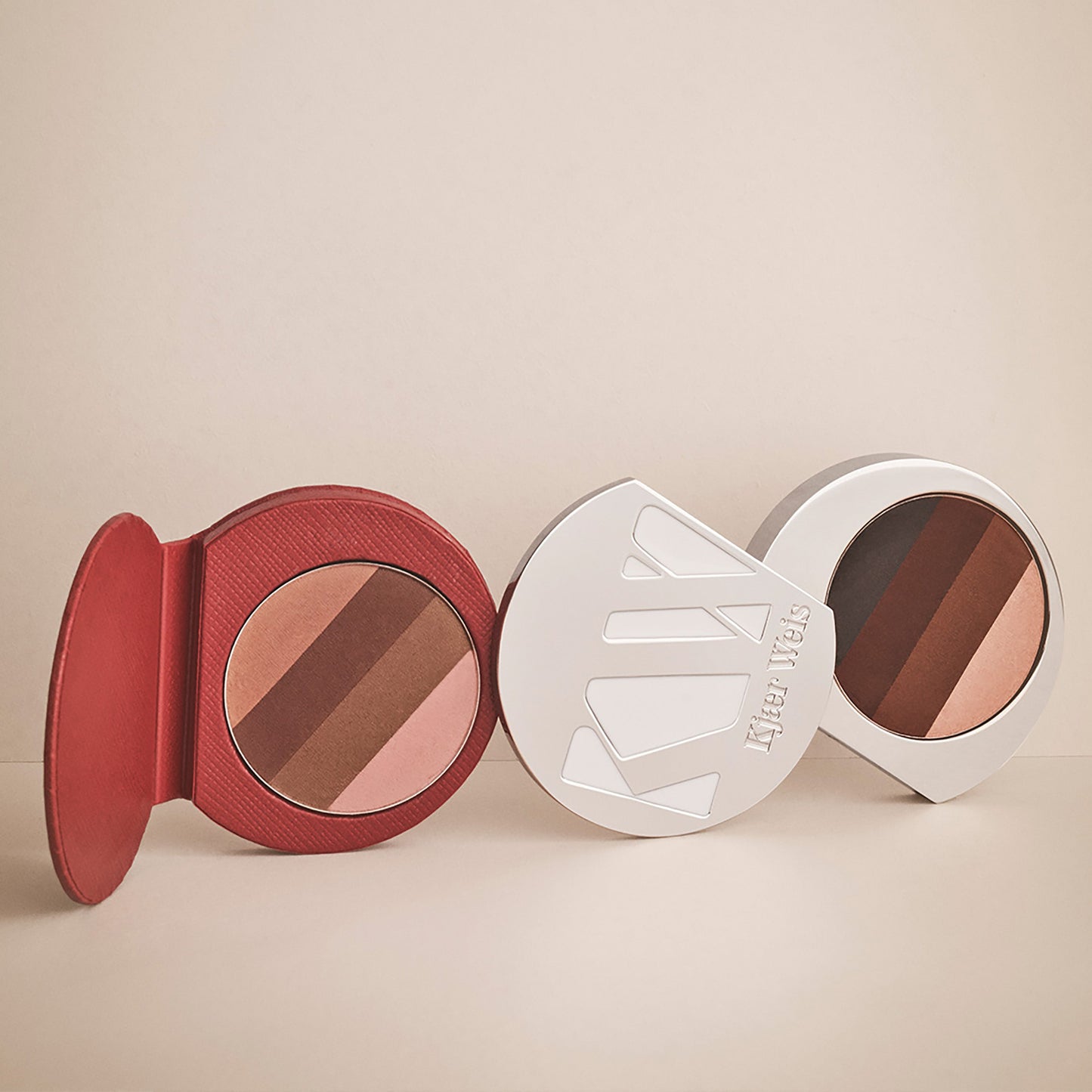 Red KW palette lying on it side next to the solid metal KW palette. Both are open to show the eye shadow quadrants inside.