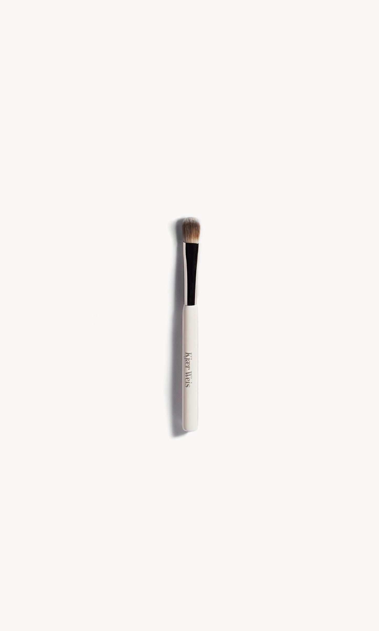 Eye shadow brush lying flat on a white background. The brush has a white and silver handle with brown bristles.