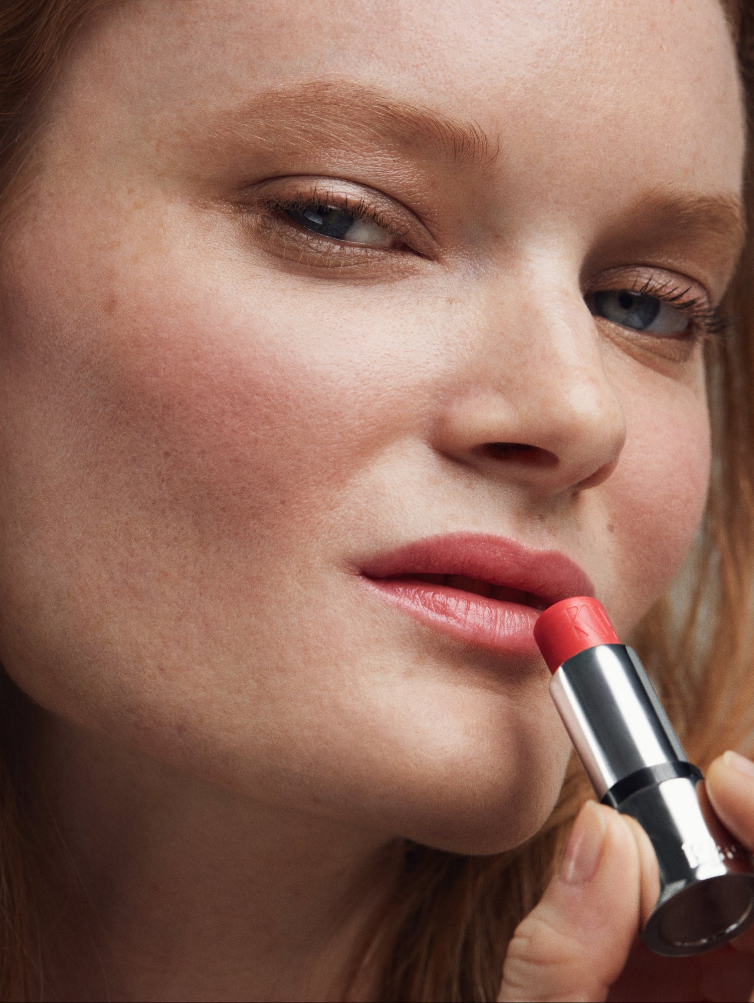 Close-up of a person applying coral Tinted Lip Balm with a neutral background