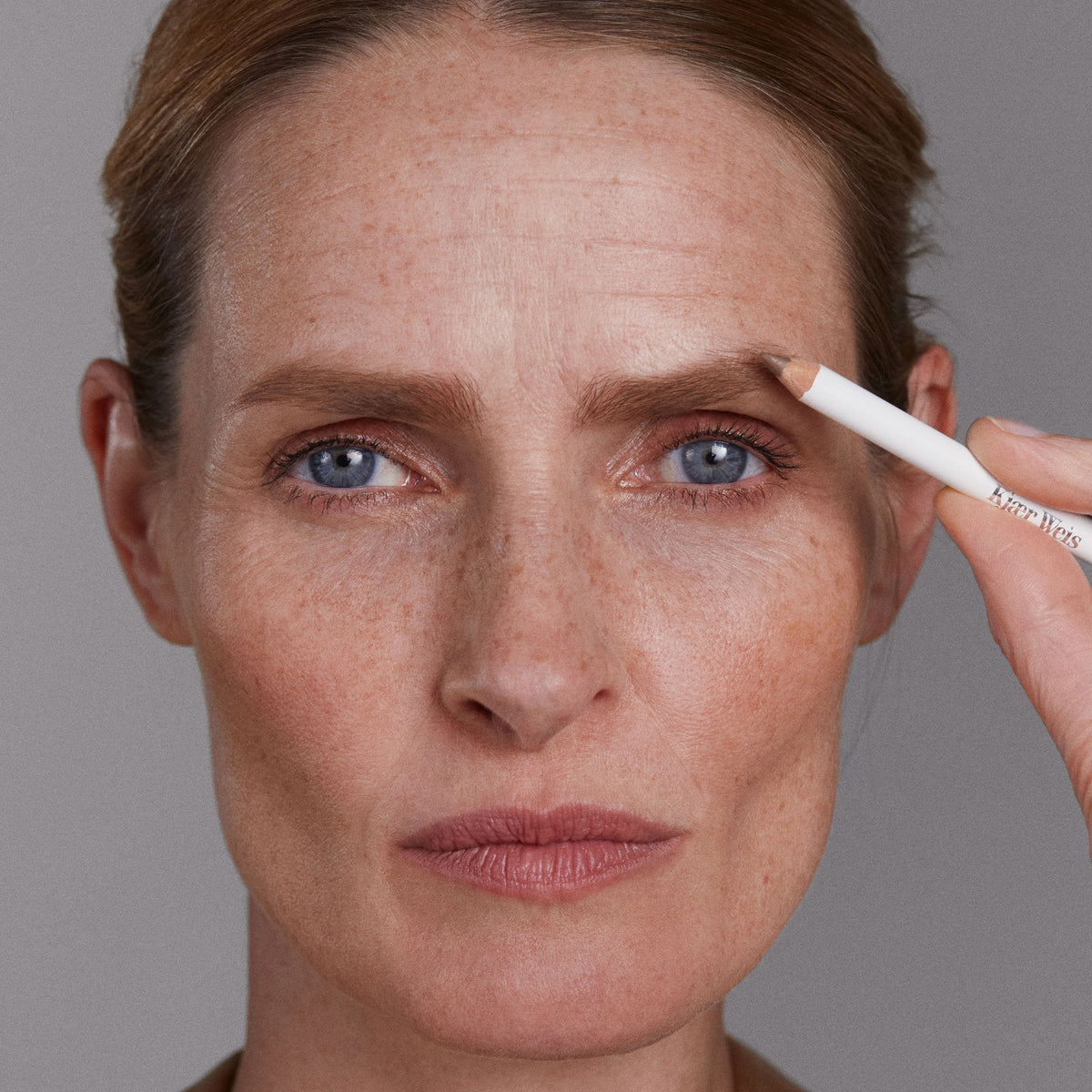Close-up of a woman applying eyebrow makeup with a blonde pencil.