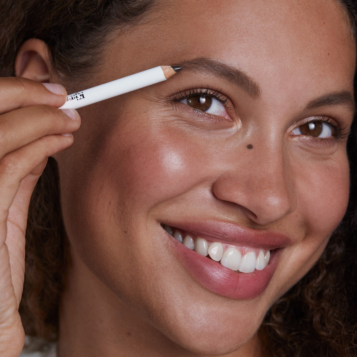 Close-up of a woman applying eyebrow makeup with a deep brown pencil.