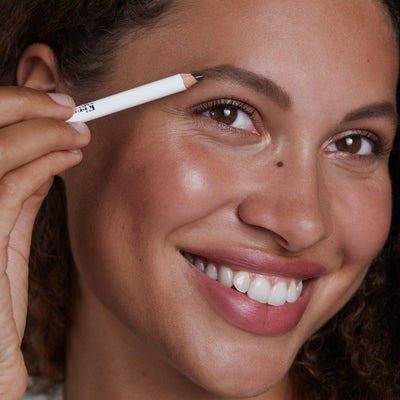 Close-up of a woman applying eyebrow makeup with a deep brown pencil.