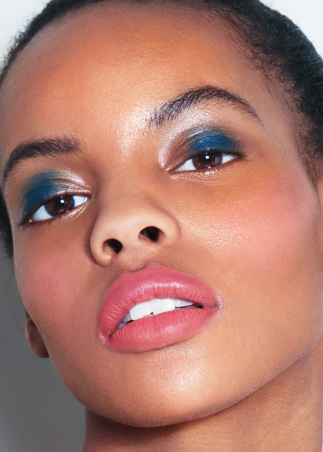 Close-up of a model's face showcasing makeup, featuring vibrant blue eyeshadow on the eyes and a soft pink lipstick on the lips.