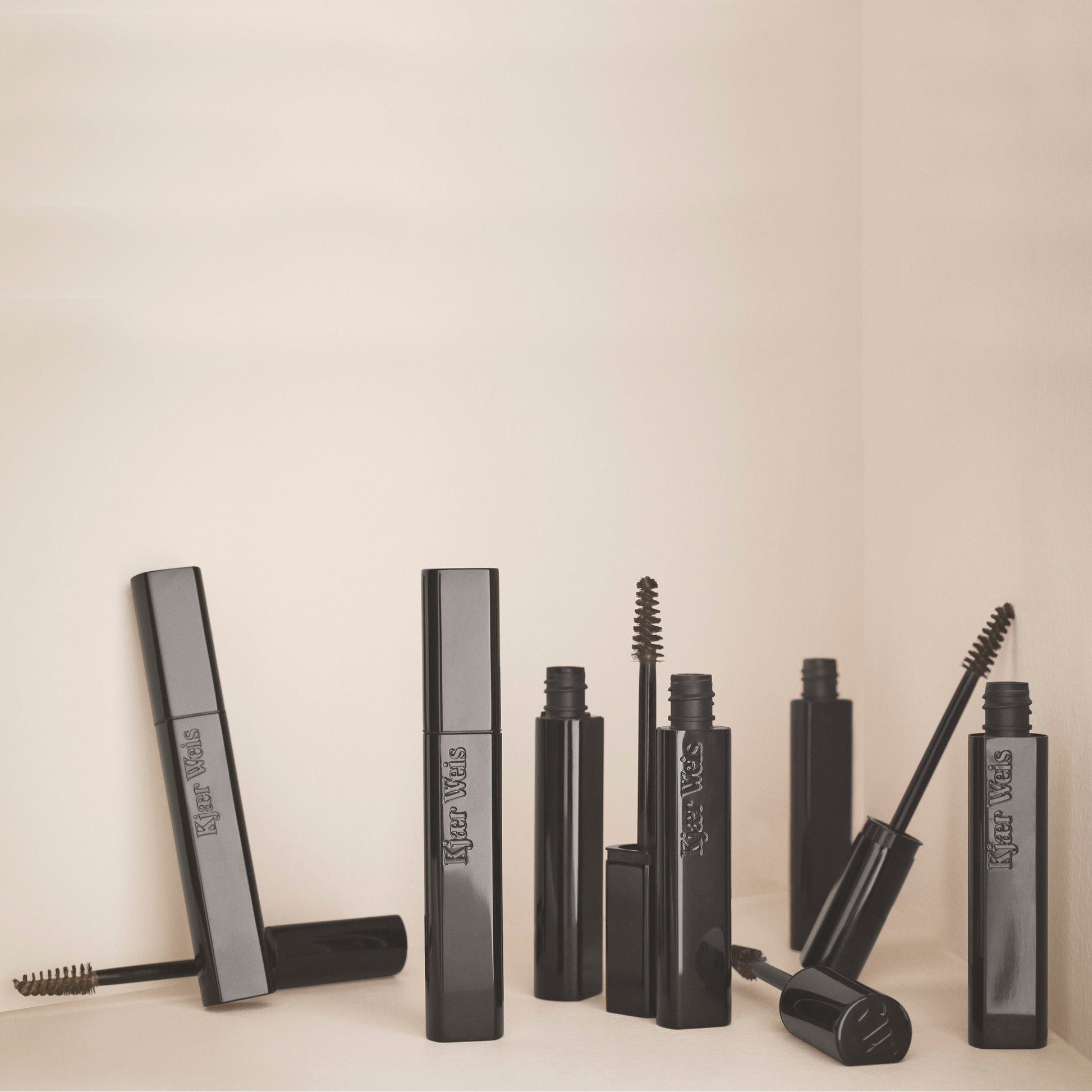 various kjaer weis brow gel wands and cases in glossy black material against a beige background