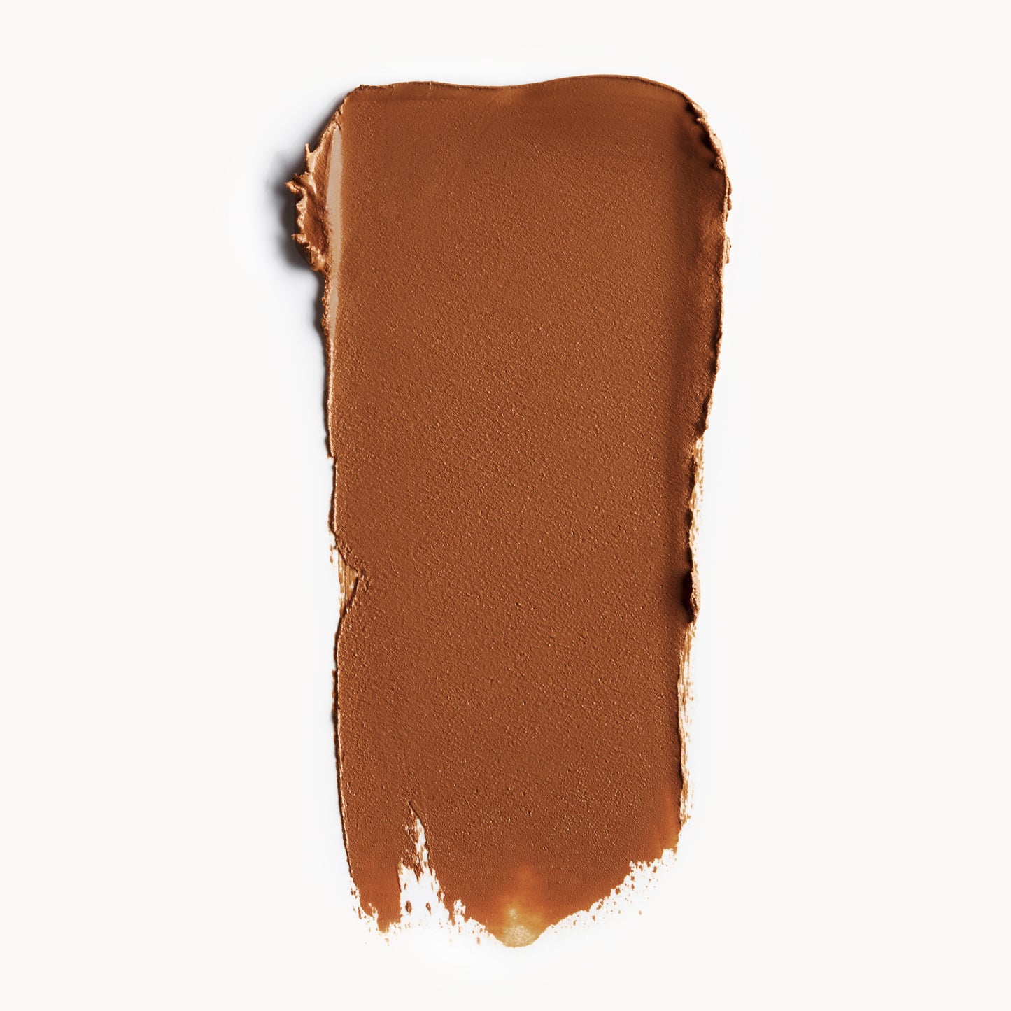A wipe of deep, warm-toned cream foundation on a white background