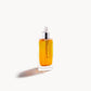 Glass bottle with white pipette top and gold-coloured liquid inside on a white background