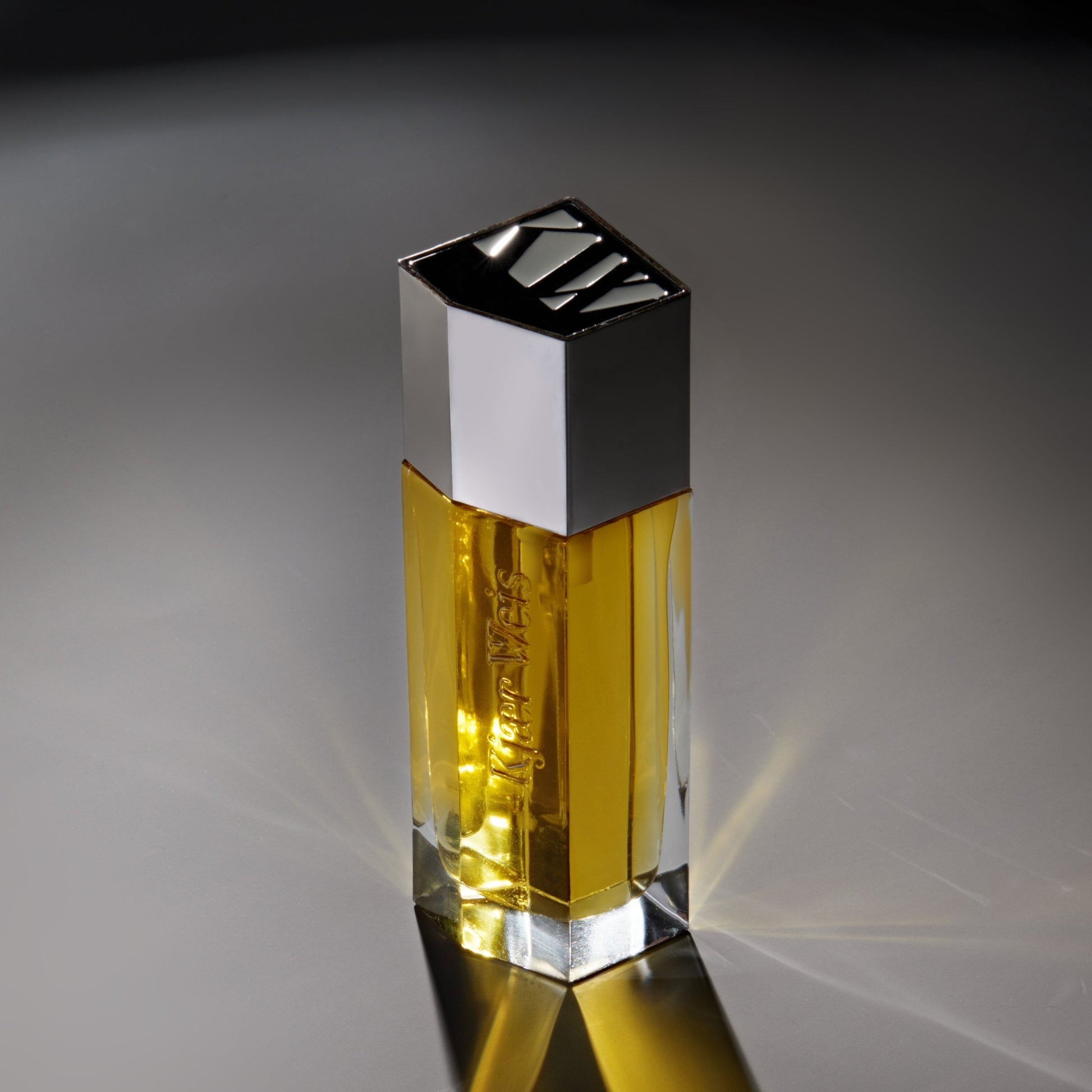 Kjaer Weis body oil in glass bottle reflecting light on a grey background
