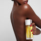 A woman holds a bottle of Kjaer Weis body oil against her body