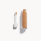 An open bottle of concealer on its side next to a white refill wand