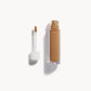 Alt text: An open bottle of concealer on its side next to a white refill wand