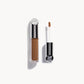 Kjaer Weis concealer in a clear bottle with silver metal top next to the concealer wand