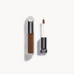 Kjaer Weis concealer in a clear bottle with silver metal top next to the concealer wand