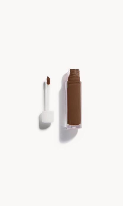 An open bottle of concealer on its side next to a white refill wand