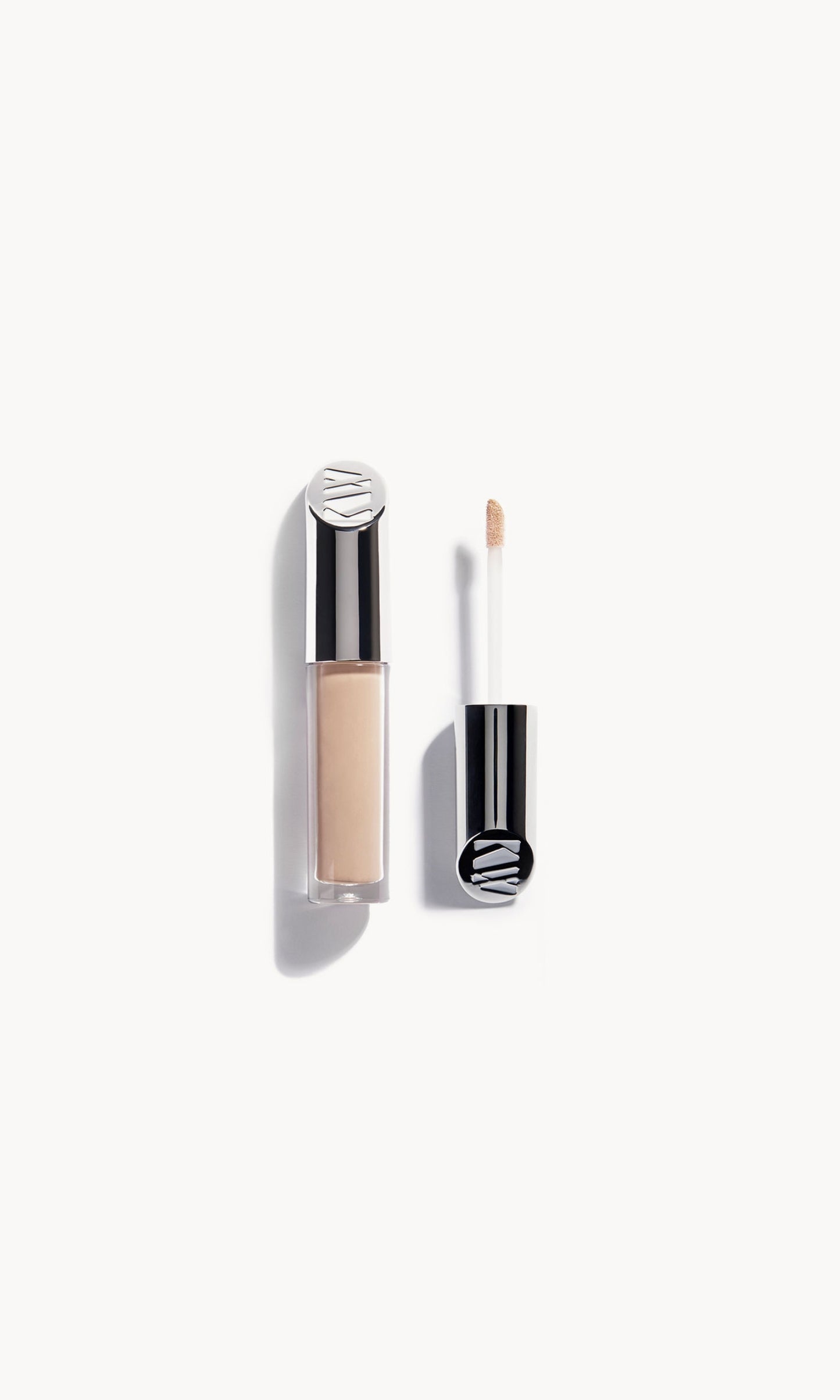 Kjaer Weis concealer in a clear bottle with silver metal top next to the concealer wand