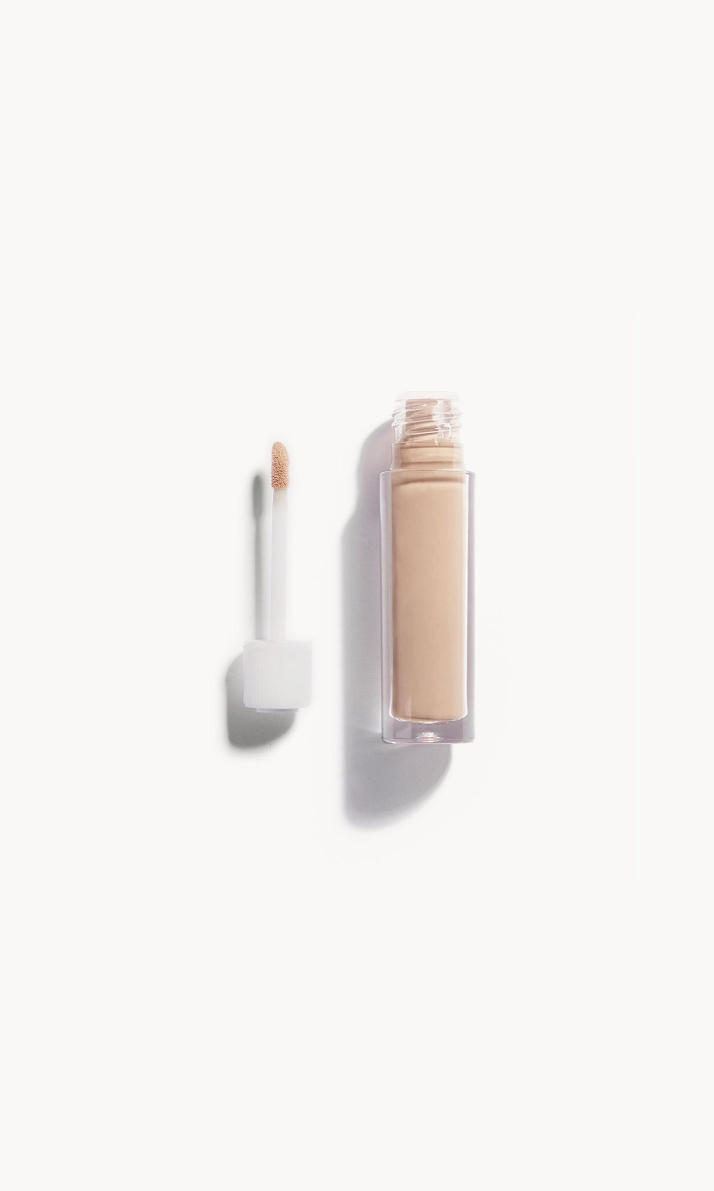 An open bottle of concealer on its side next to a white refill wand