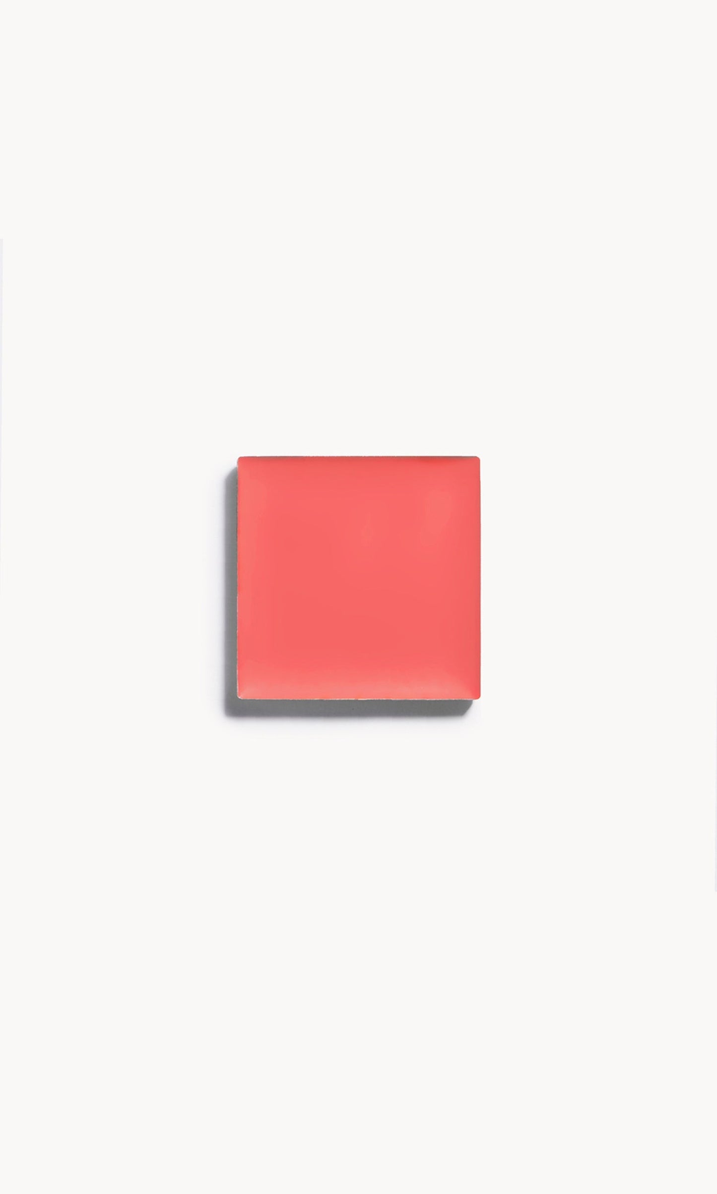 A square of bright coral cream blush on a white background