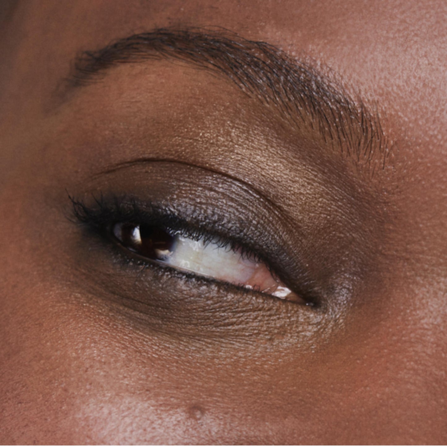 Close up of person’s eye with a deep skin tone wearing cream eye shadow