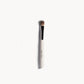 Eye shadow brush lying flat on a white background. The brush has a white and silver handle with brown bristles. 