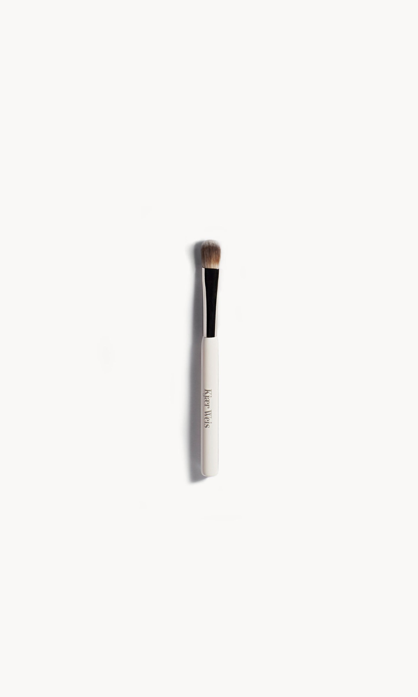 Eye shadow brush lying flat on a white background. The brush has a white and silver handle with brown bristles. 