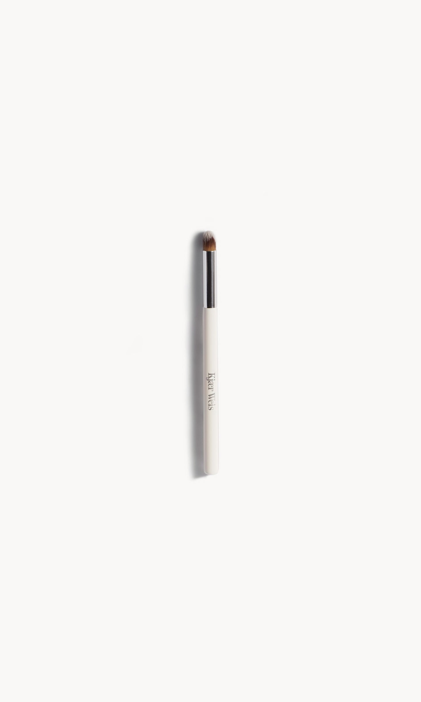 Eye makeup brush with white and silver handle, and short brown bristles on a white background
