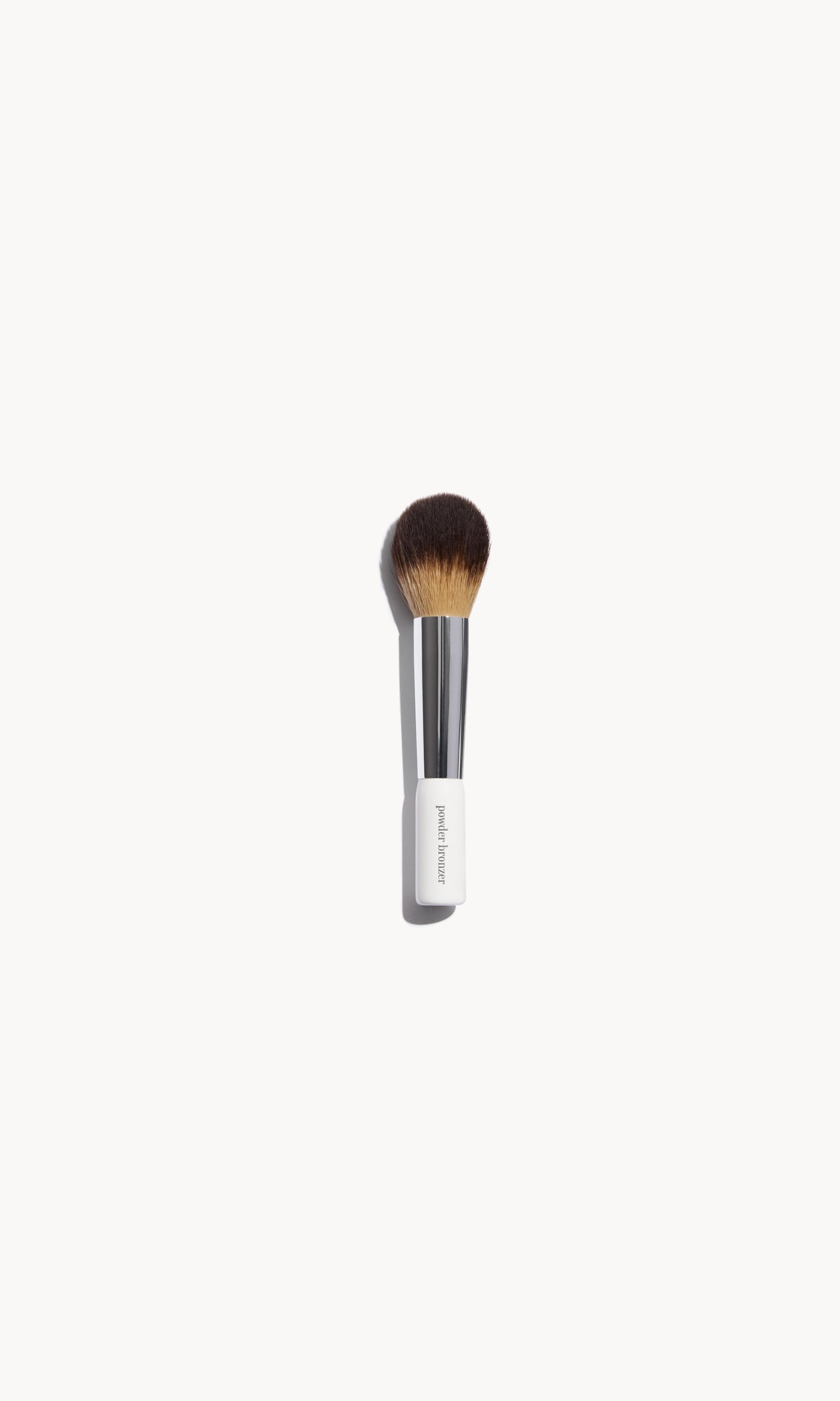 Makeup brush with white and silver handle and large rounded bristles on a white background